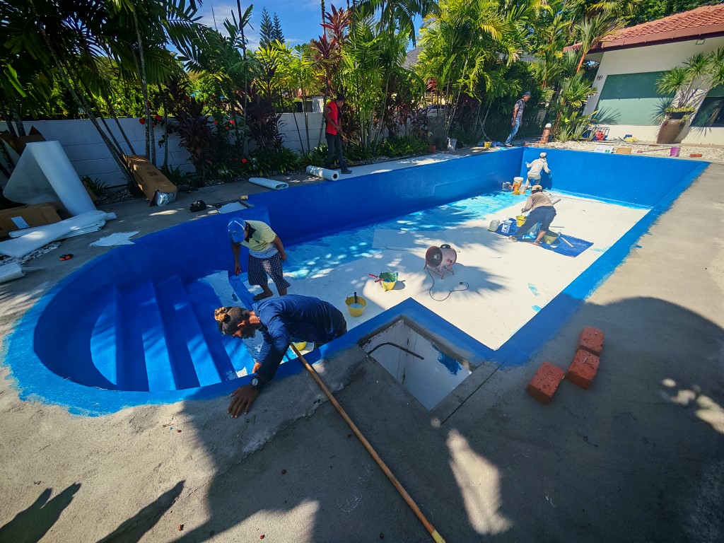 A crew of pool repair specialists rolling bright blue FRP fiberglass laminate onto the floors and stairs of an empty residential concrete swimming pool.